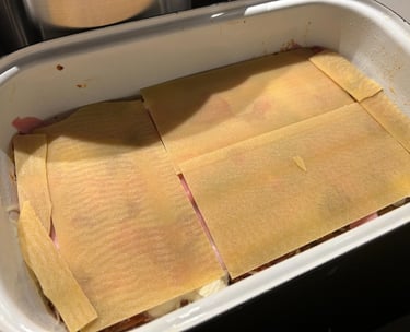 Uncooked lasagna layered with pasta sheets, ham, and sauce in a white baking dish, ready for baking.