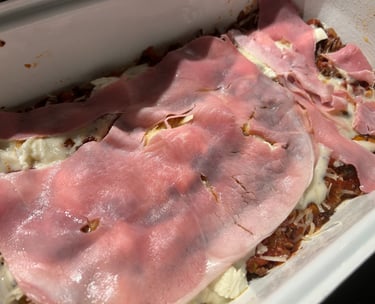 Homemade lasagna layers featuring savory meat sauce, white cheese, and thin slices of pink ham.