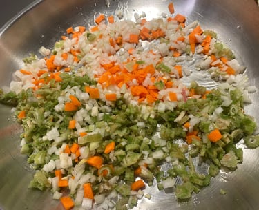 Finely diced carrots, celery, and onions sautéing as a mirepoix base in a stainless steel pan.