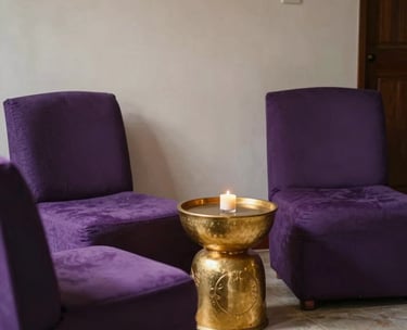 A comfortable seating area for clients in a South American spiritual center. Plush purple chairs, a golden side table, and a feeling of privacy and safety.
