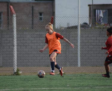 Female soccer player in an orange training vest dribbling the ball during a practice session.