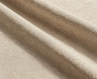 Close-up photography of a high-end textured linen fabric in soft beige tones, natural sunlight creating subtle shadows, editorial style, Spanish-speaking aesthetic.