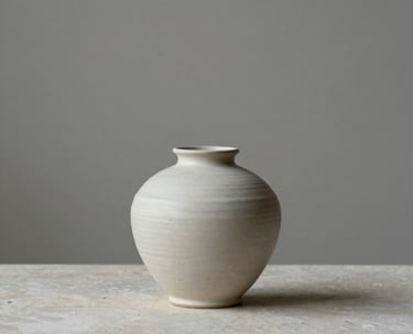 Minimalist interior detail featuring a ceramic vase on a stone surface, neutral gray and off-white tones, soft natural lighting, serene atmosphere.