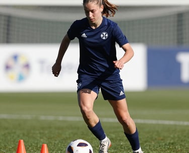 A focused European teenage girl practicing dribbling around cones, displaying high intensity, dressed in professional training gear with Total Football Academy logo details, bright daylight.