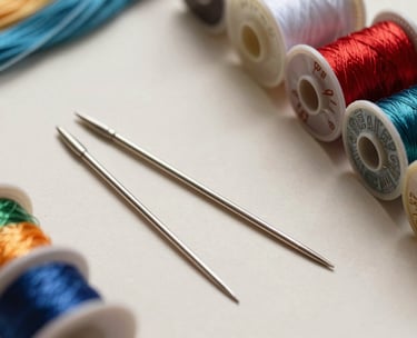 A professional flat-lay photograph of traditional embroidery tools including silver needles, Zari wire, and colorful silk spools on a light cream surface.