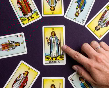 A top-down view of a spread of Tarot cards on a dark purple surface, with a delicate hand wearing a silver ring pointing to a card, South American style.