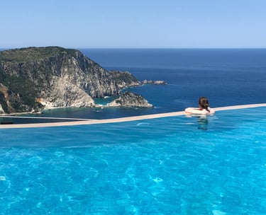 Person relaxing in a luxury infinity pool overlooking a rugged coastal cliff and blue ocean.