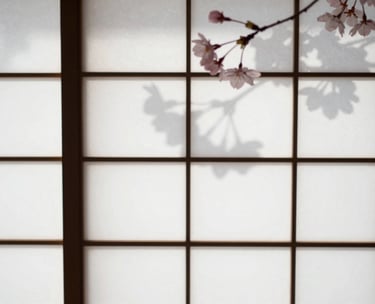 A high-detail close-up of a white paper shoji screen with the soft, elegant shadow of a cherry blossom branch cast upon it from the sun. Minimalist, zen aesthetic with soft pink and gray tones.