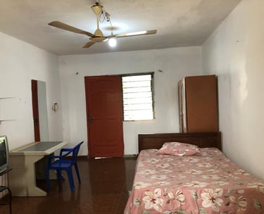 Basic guest room featuring a single bed with floral sheets, ceiling fan, and wooden furniture.