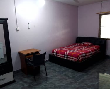 A simple bedroom featuring a bed with red plaid bedding, a wooden desk with a black chair, and a wardrobe.