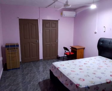 A studio with light purple walls, a bed with floral sheets, and a wooden study desk, fridge.