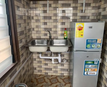Double bowl stainless steel kitchen sink and silver Nasco refrigerator in a tiled room.