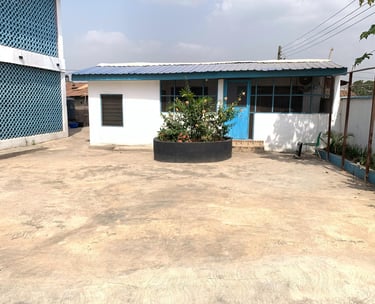 Small white building with blue doors and trim next to a courtyard with a circular stone planter.