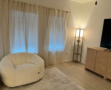 Cozy living room with a white sherpa bean bag chair, linen curtains, and a wooden TV stand.