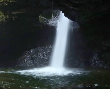 A scenic underground waterfall cascading through a dark rocky cave into a natural pool.