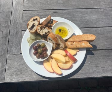A snack plate of apples, bread, olives, pickles, and biscotti 