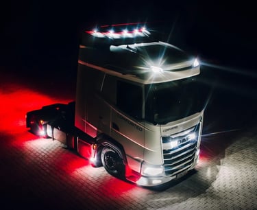 White DAF semi-truck with illuminated headlights and red underglow lighting parked on a stone lot at night.