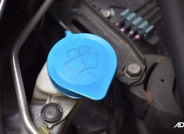 A blue windshield wiper fluid reservoir cap located inside a car engine bay for vehicle maintenance.