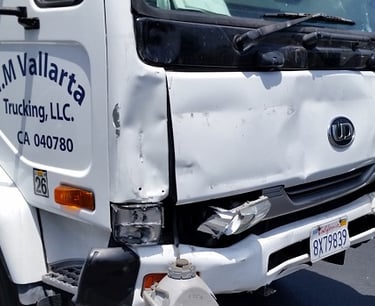 White commercial delivery truck with front end damage to the bumper and hood after a vehicle accident.