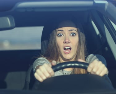 Scared woman driver looking shocked and terrified behind the steering wheel while driving a car.