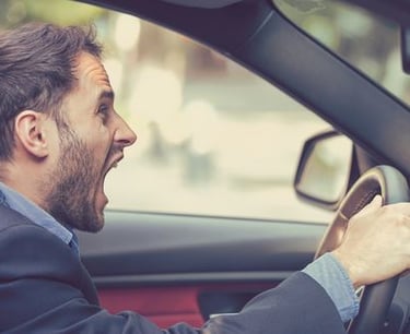 Angry businessman screaming behind the steering wheel while experiencing road rage during commute.