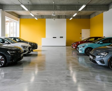 Modern car showroom with rows of new vehicles parked on a polished concrete floor against a yellow accent wall.