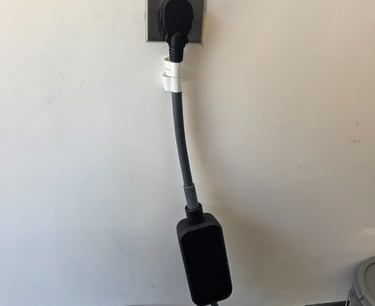 Black electric vehicle charging cable plugged into a NEMA 14-50 wall outlet for home EV charging.