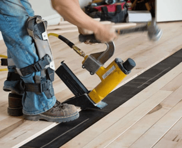 Professional installer is installing hardwood flooring with a nail gun.