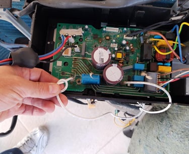 A technician repairing a damaged HVAC circuit board with capacitors and wiring components.