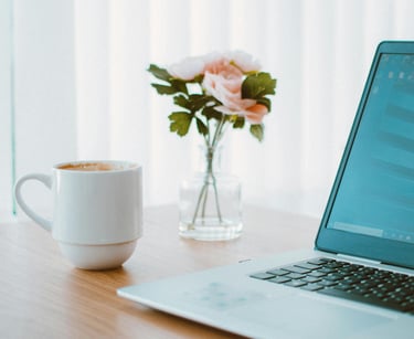 Arbeitsplatz mit Laptop, Kaffeetasse und einer Vase mit Blumen auf einem Holztisch.