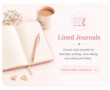 An open pink lined journal on a desk with a gold pen, coffee cup, and flowers for note-taking.