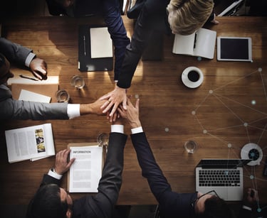 Overhead view of a business team joining hands over a boardroom table for a successful partnership.