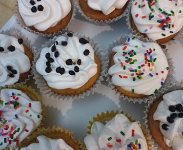 Freshly baked cupcakes with white swirl frosting topped with chocolate chips and colorful rainbow sprinkles.