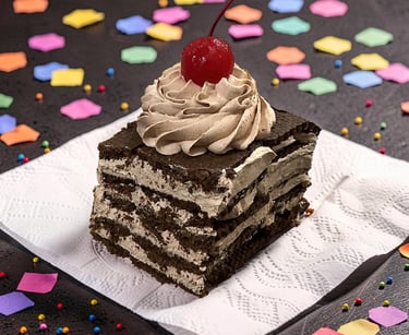 A chocolate layered cake slice with whipped cream frosting and a cherry on top with colorful confetti.