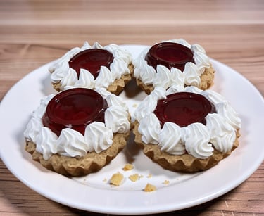 Four strawberry jelly tarts with whipped cream frosting on a white plate over a wooden table.