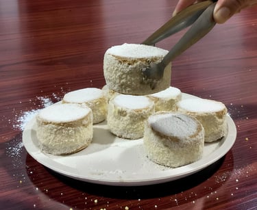 A hand using metal tongs to pick up a powdered sugar Alfajor cookie from a white plate.