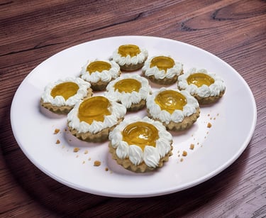 Mini fruit tarts with whipped cream swirls and apricot glaze on a white plate over a dark wood table.