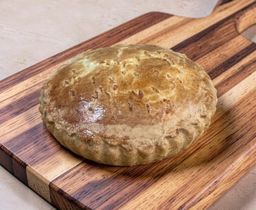 Golden brown homemade meat pie on a wooden cutting board with crimped crust edges.