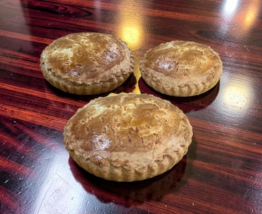Golden brown, baked empanada or savory pie on a striped wooden cutting board, showcasing its flaky pastry crust.