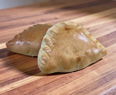 Two golden brown baked empanadas with crimped edges on a wooden cutting board.