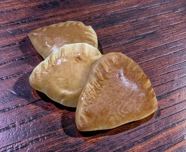 Golden brown baked empanadas with crimped edges on a dark wood grain table.
