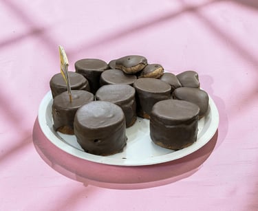 A white plate filled with gourmet chocolate covered marshmallows on a pink background.