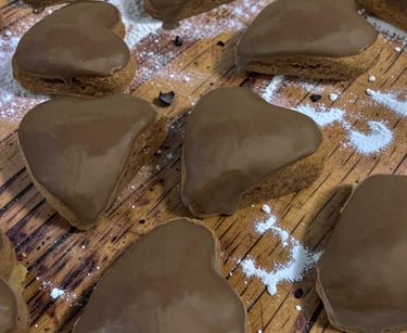 Heart-shaped gingerbread cookies with smooth chocolate icing on a wooden board with powdered sugar.