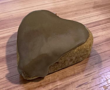 A heart-shaped gingerbread cookie with smooth brown icing on a light wood grain surface.
