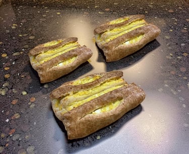 Three freshly baked Finnish karelian pastries with egg butter on a dark stone countertop.