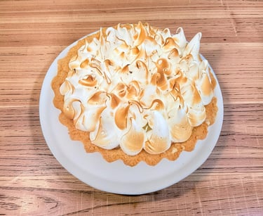 Homemade lemon meringue tart with toasted peaks on a white plate over a wooden table.