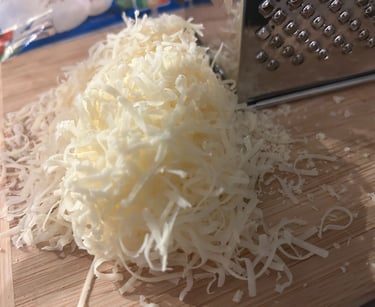 Freshly grated parmesan cheese piled on a wooden cutting board next to a stainless steel box grater.