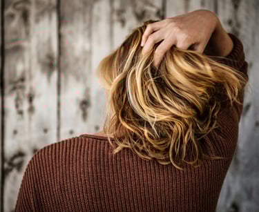 Vista trasera de una mujer con balayage rubio ondulado pasando los dedos por su cabello.