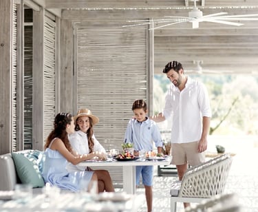 A happy family enjoys a luxury outdoor brunch at Ikos Aria a sunlit beach resort patio.