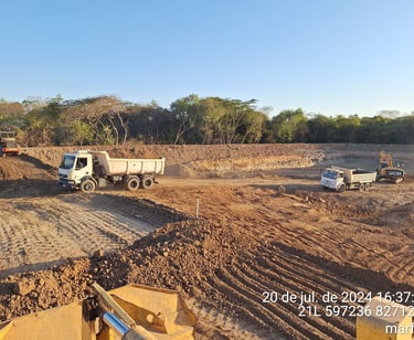 Canteiro de obras com caminhões basculantes e terraplanagem em execução em área aberta no MT